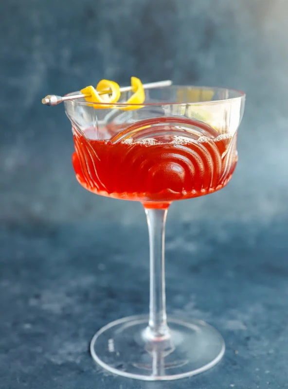 easy aperol bourbon cocktail in coupe glass with lemon peel garnish