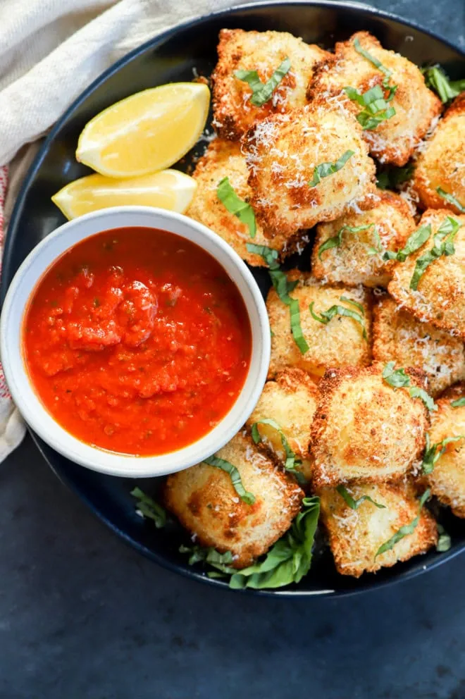 air fryer ravioli on plate with lemon slices, marinara sauce, and fresh basil