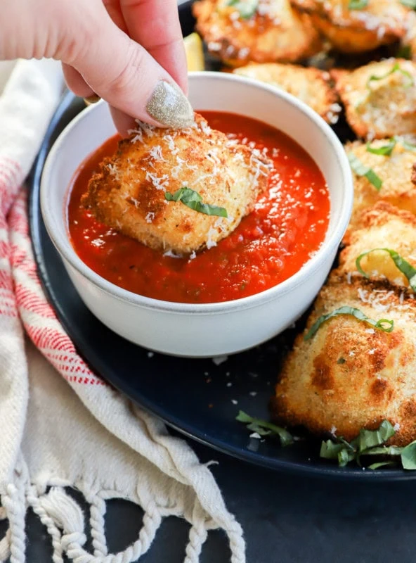 hand dipping the ravioli into sauce with fresh herbs