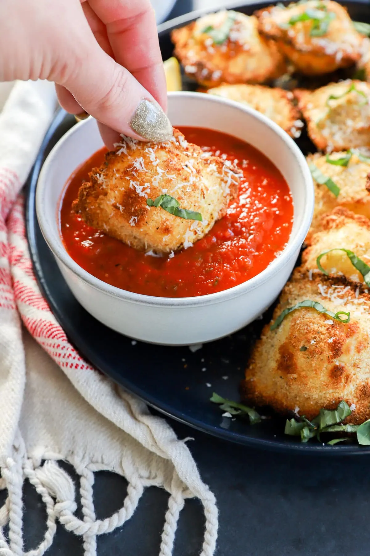 hand dipping the ravioli into sauce with fresh herbs