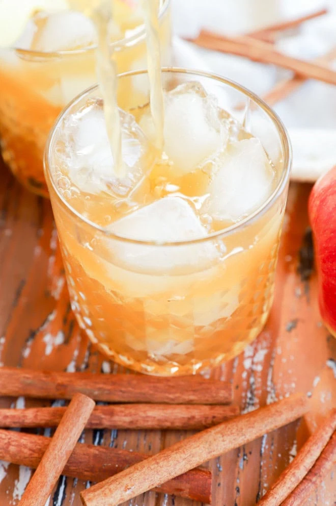 straining apple cider cocktail in cocktail glass filled with ice