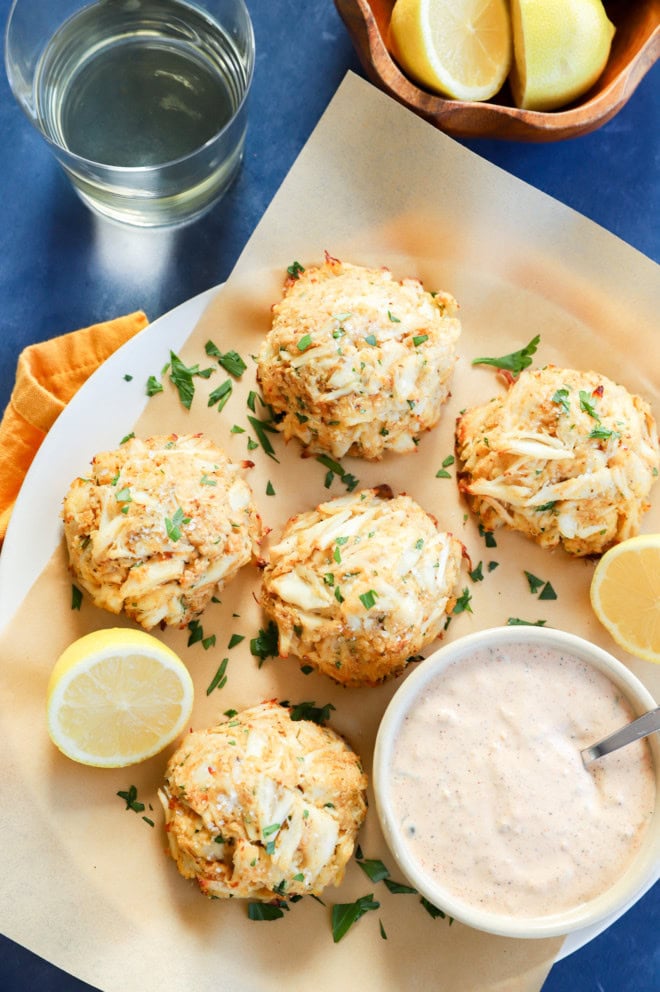 baked crab cakes on lined platter with sauce and lemons and white wine