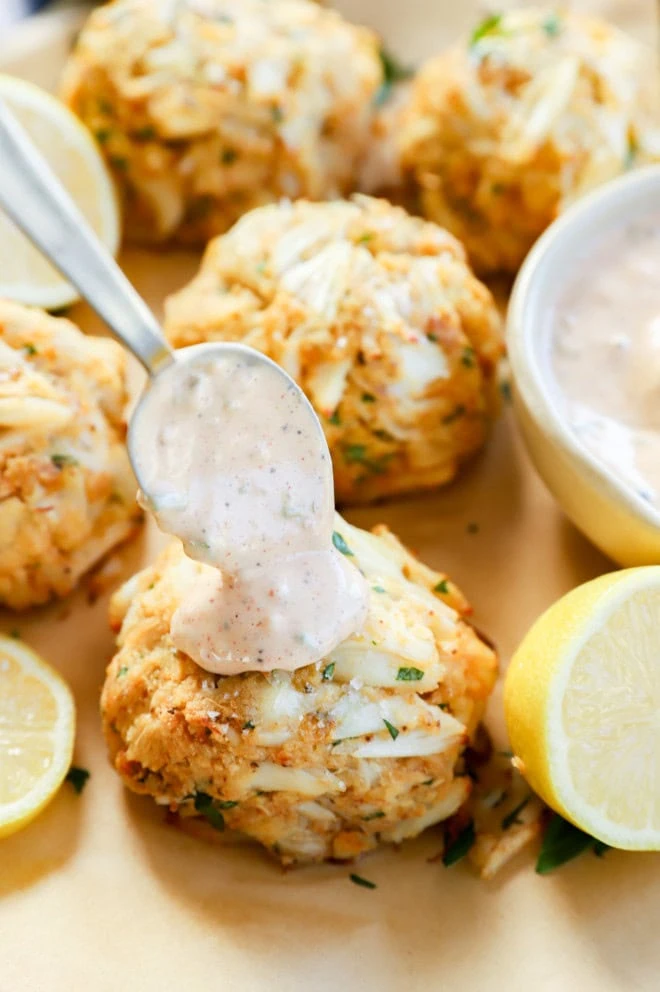 spooning sauce onto baked seafood appetizer with fresh lemons