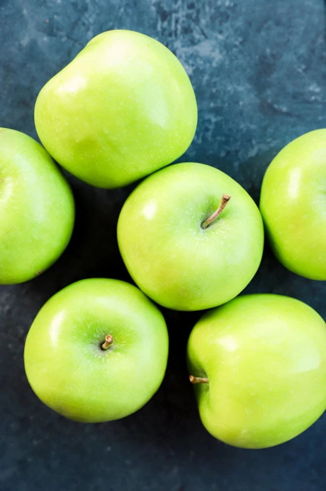 fresh green whole apples in a pile on black background