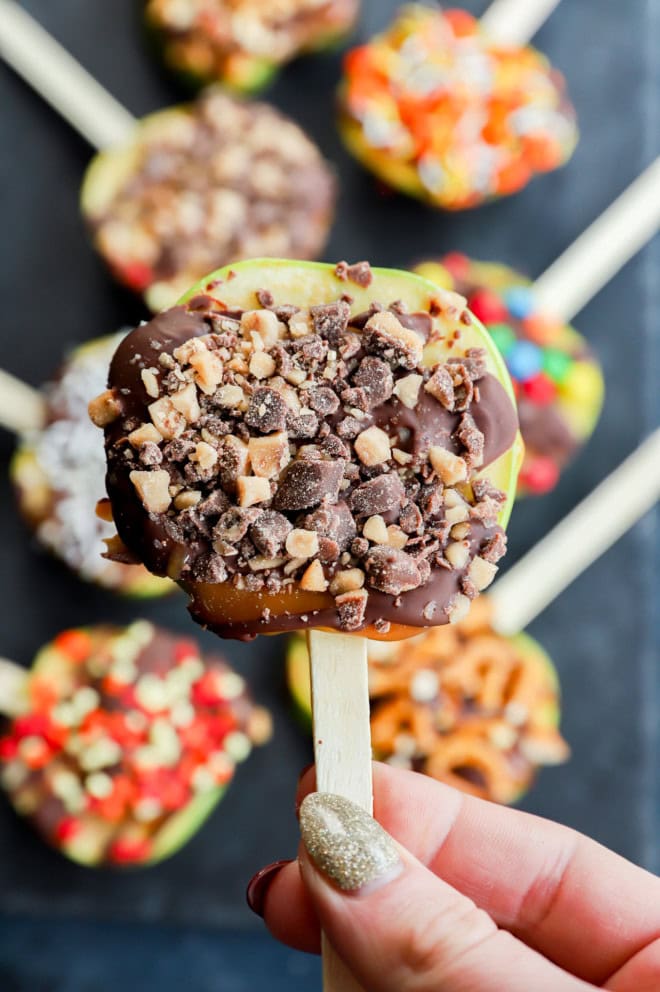 hand holding a candy apple slice with toffee bits on it