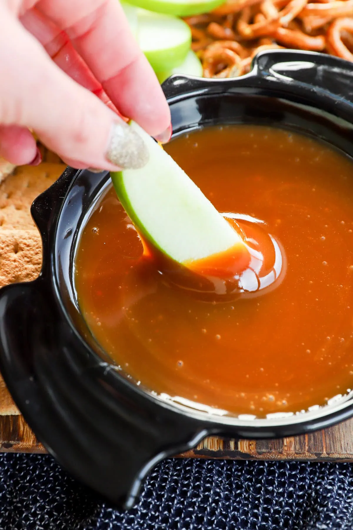 hand dipping an apple slice in caramel apple dip in a bowl