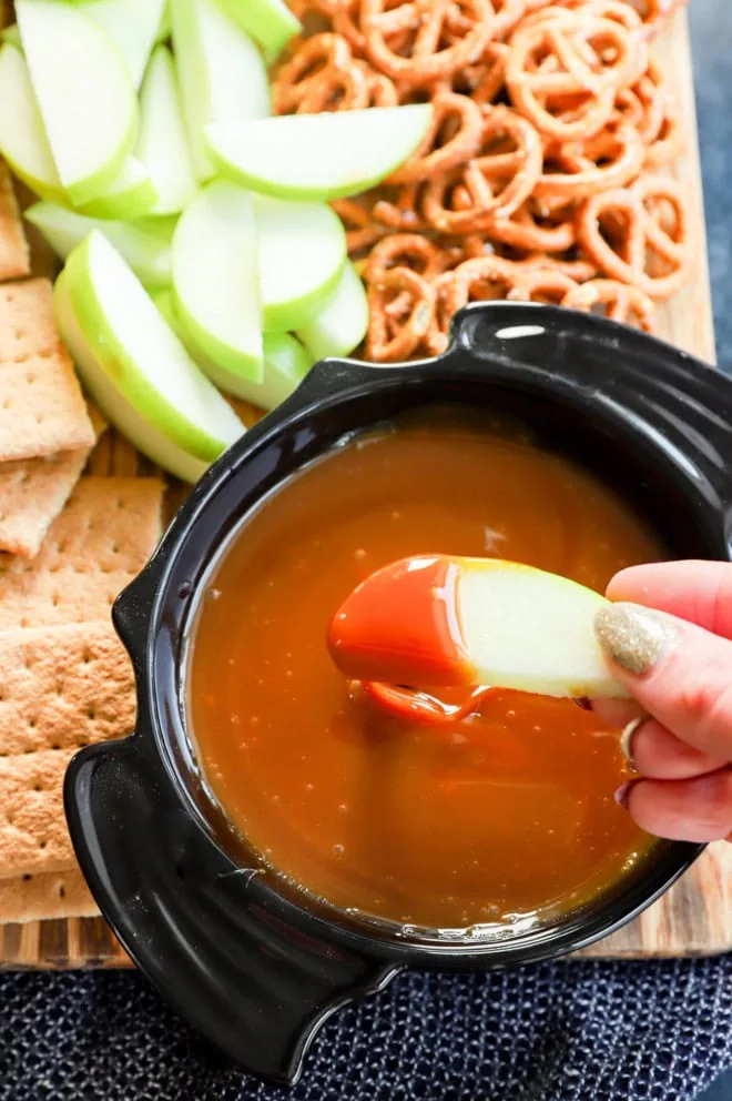 hand dipping apple into a sweet sauce in a bat bowl with other dippers on a platter