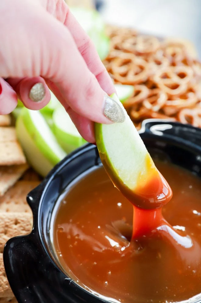 hand dipping fruit into a sweet sauce in a bowl