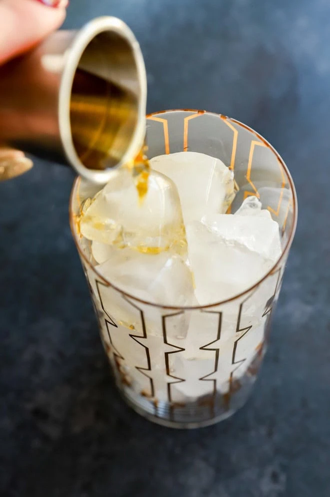 Pouring whiskey into a highball glass filled with ice