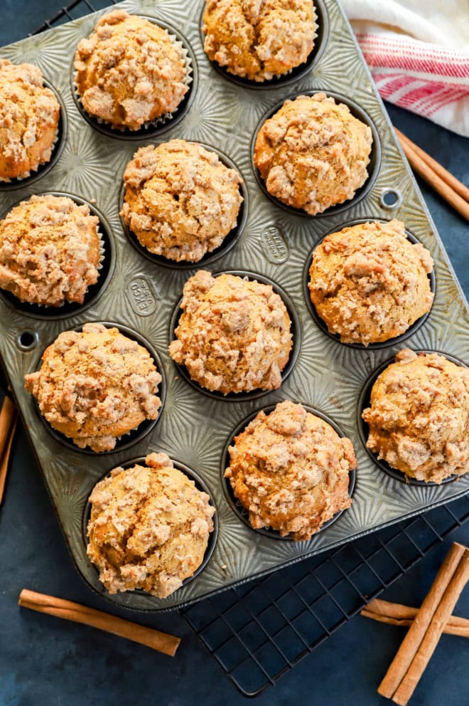 pumpkin banana muffins in muffin tin with cinnamon sticks and striped linen