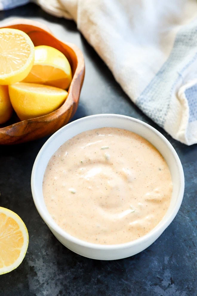 creamy seafood sauce in bowl with bowl of lemons and white linen with blue on it