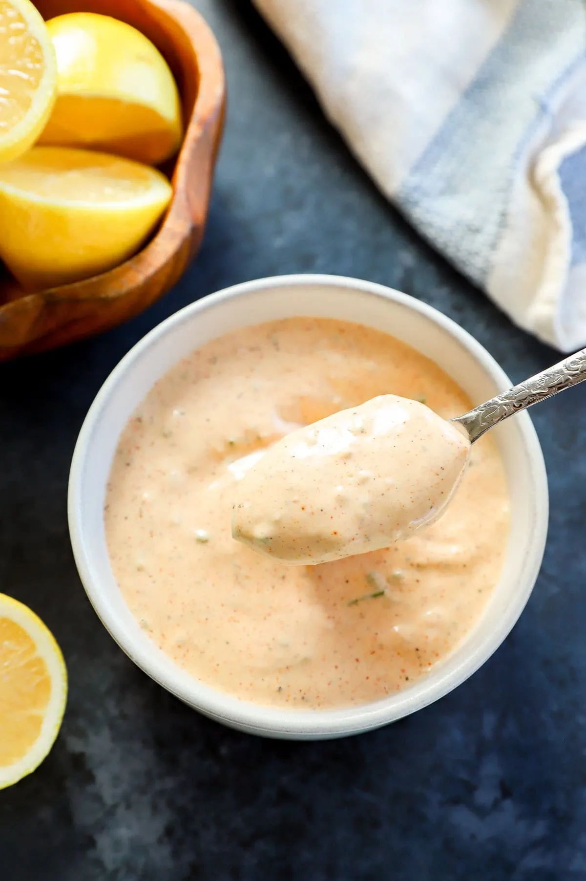 spoon lifting out sauce for crabs cakes from bowl with bowl of lemon halves