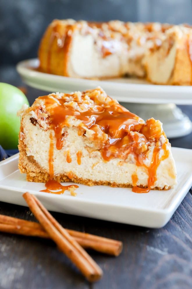 slice of caramel apple crumble cheesecake on plate with fresh apple and cinnamon sticks