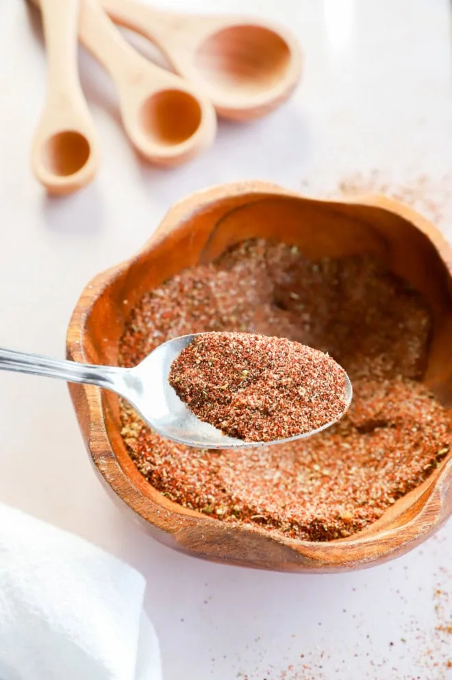 spoon lifting out chili seasoning from bowl with measuring spoons in background