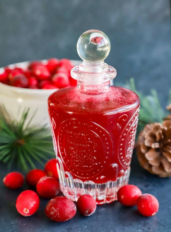 cranberry simple syrup in a jar with pinecone and frozen berries