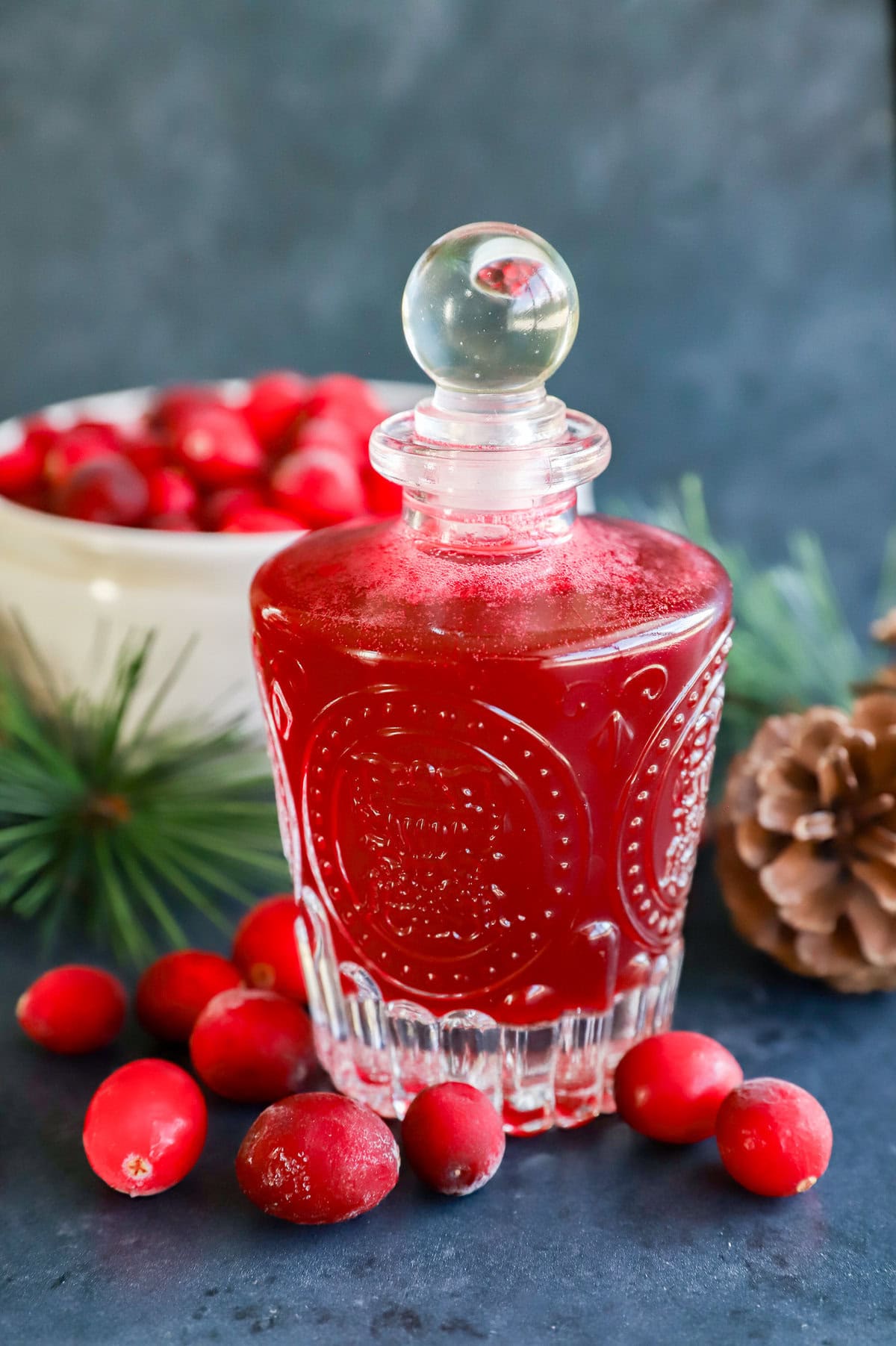 cranberry simple syrup in a jar with pinecone and frozen berries