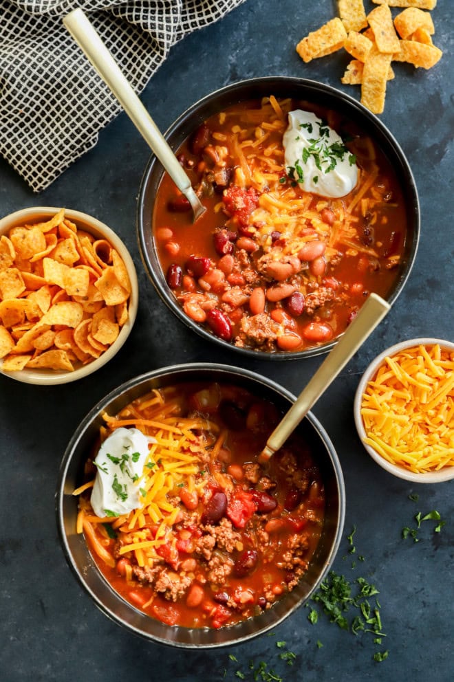 two black bowls of homemade instant pot chili with gold spoons