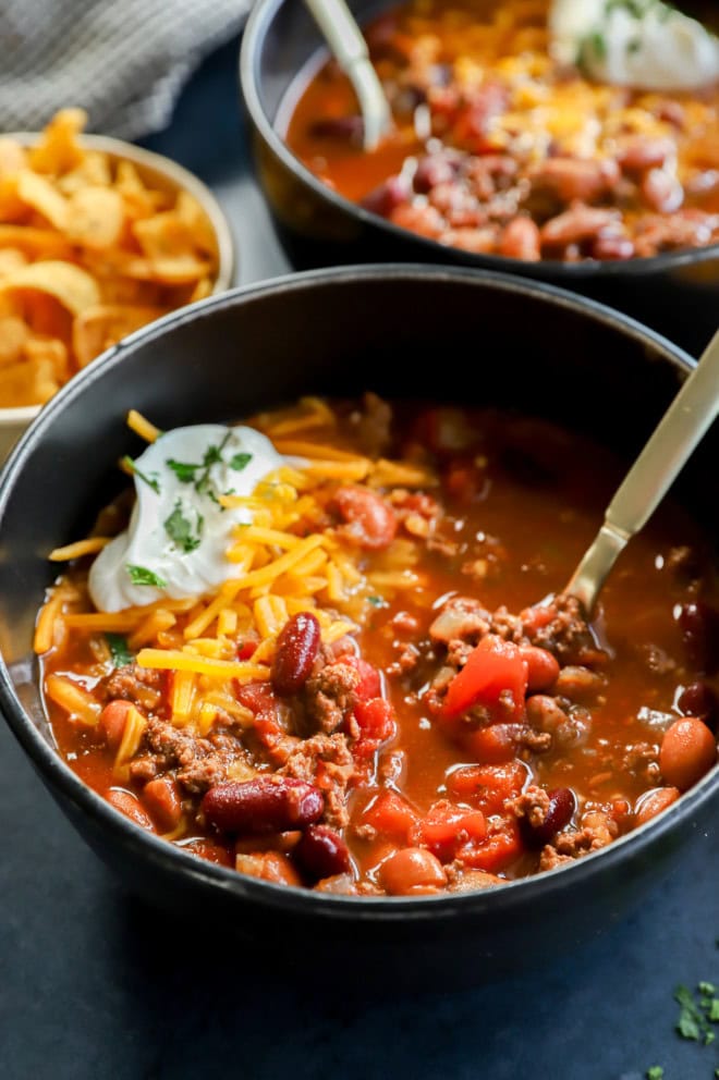 bowl of beef stew with gold spoon topped with cheeses