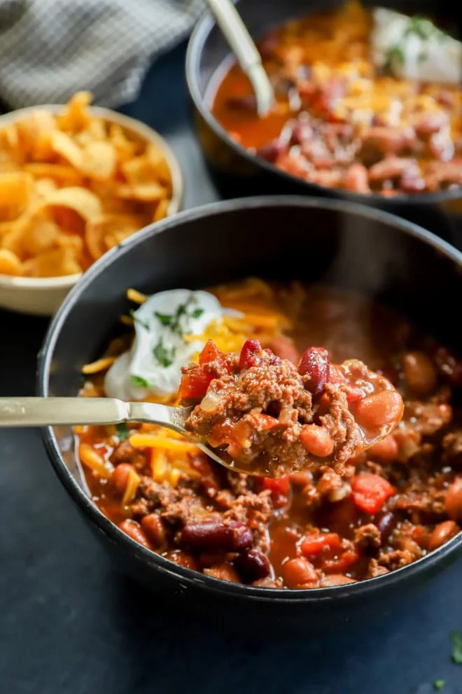 spooning out beef stew from a black bowl with a gold spoon