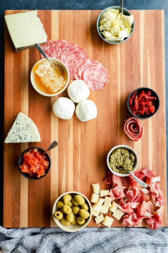 meats added to cutting board serving platter with cheeses and bowls