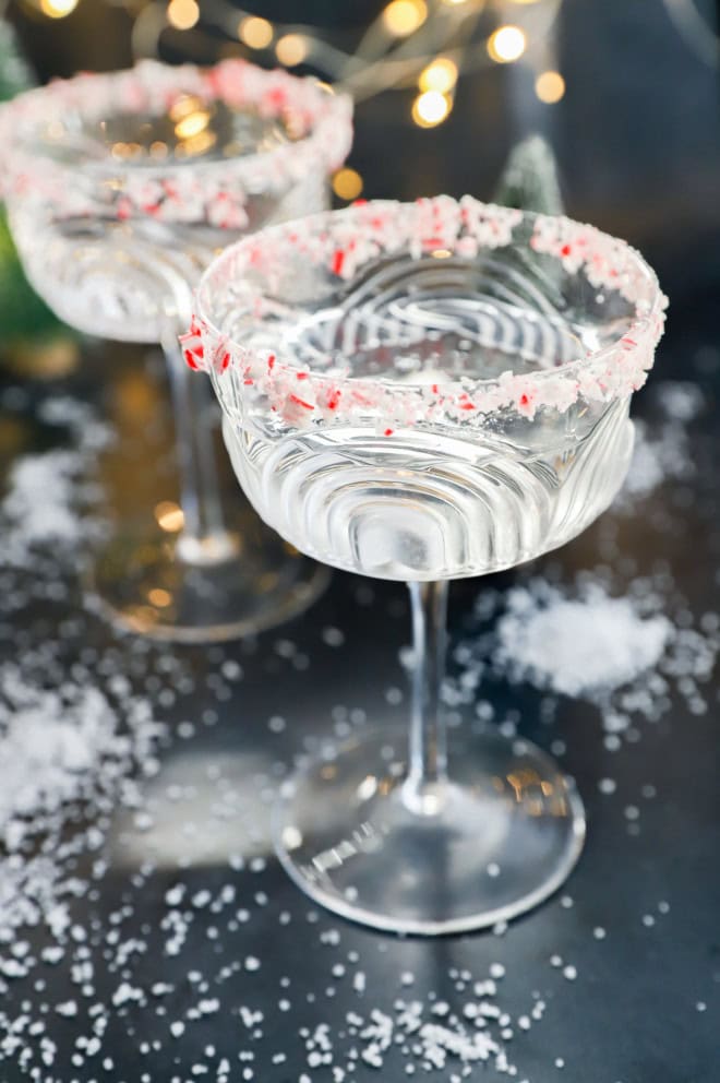 snow around cocktail glasses with candy cane cocktails in them