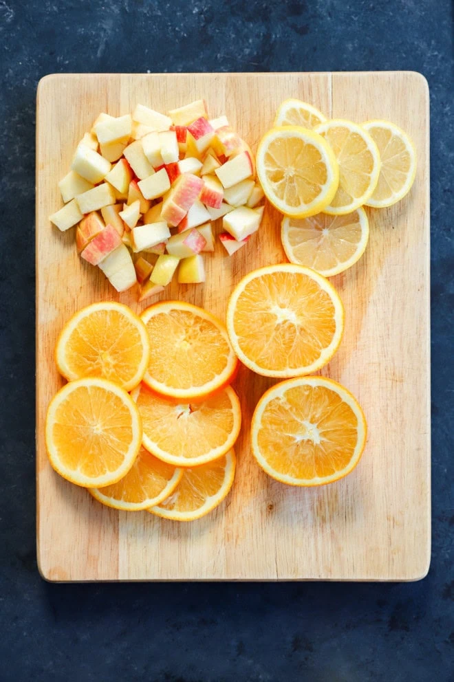 sliced oranges, sliced lemon, and chopped apple on cutting board