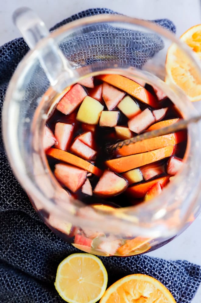 stirring a fruity punch in a large pitcher with orange halves