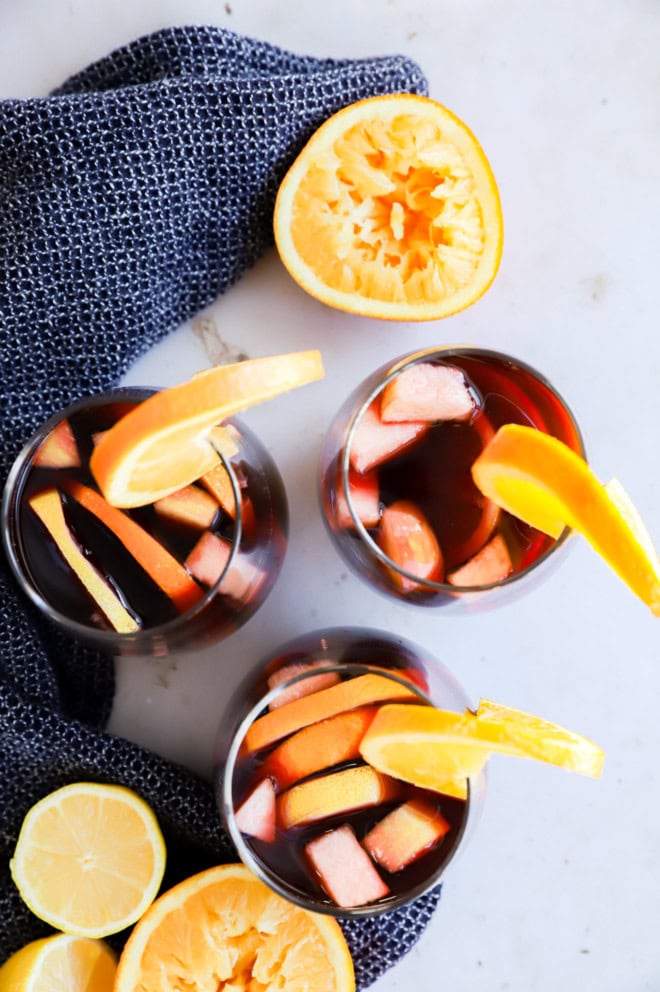 three glasses of red sangria and orange halves with linen