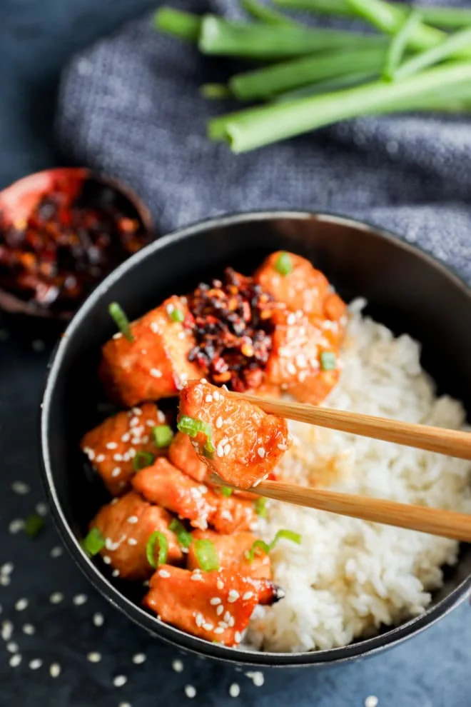 chopsticks holding a small piece of glazed salmon over salmon with rice