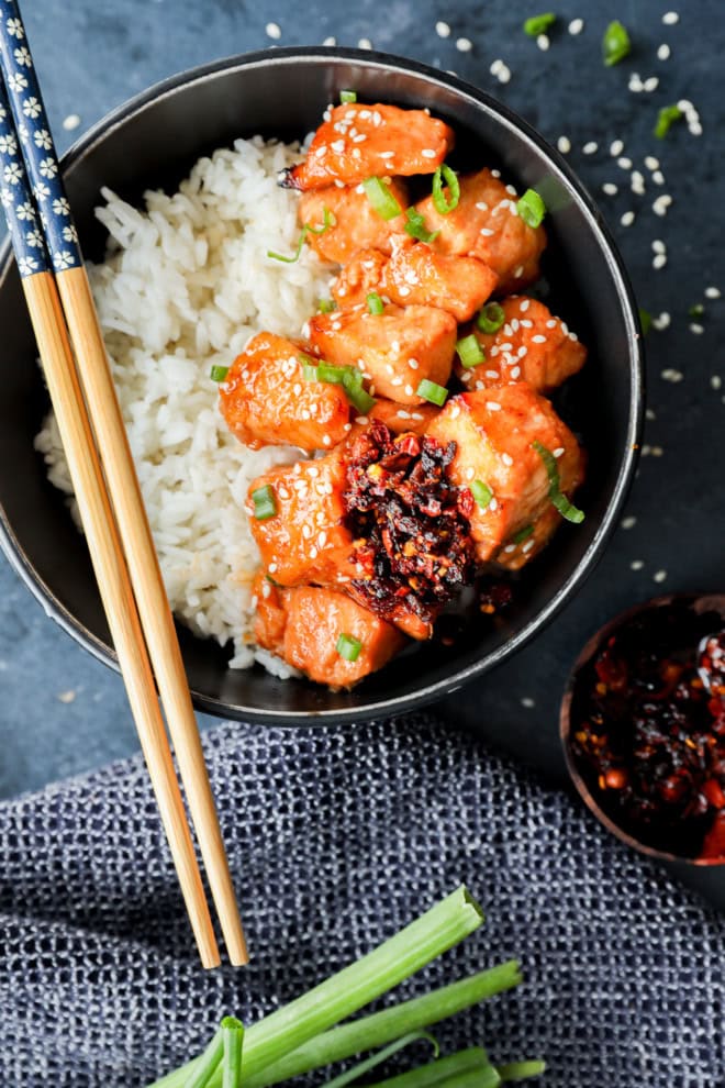 bowl of fish pieces in honey ginger glaze over rice in black bowl with chopsticks