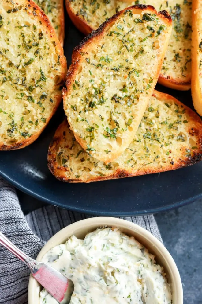 butter in bowl next to slices of sourdough garlic toast bread on a plate piled up