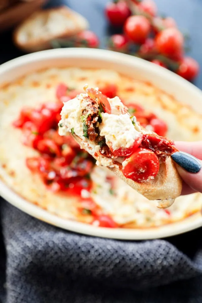 crostini with melted cheese mixture and tomatoes and fresh herbs on it