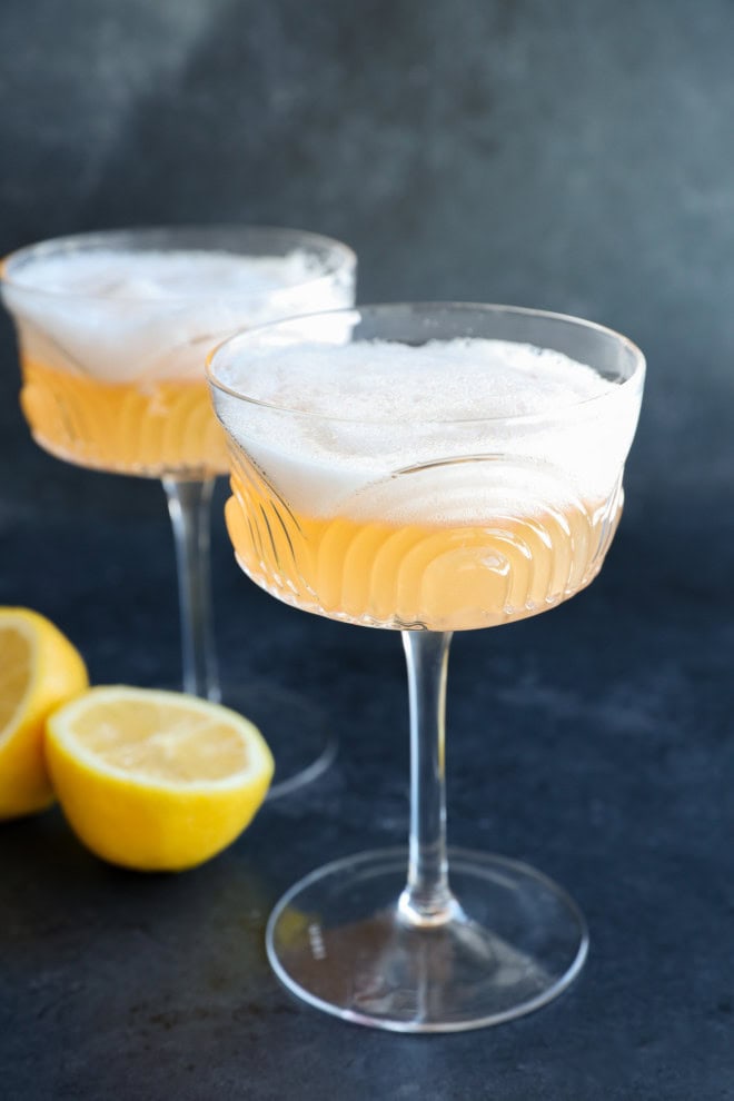 two gin sour cocktails in coupe glasses with lemon halves