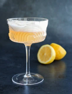 gin sour in coupe glass on black with lemon halves