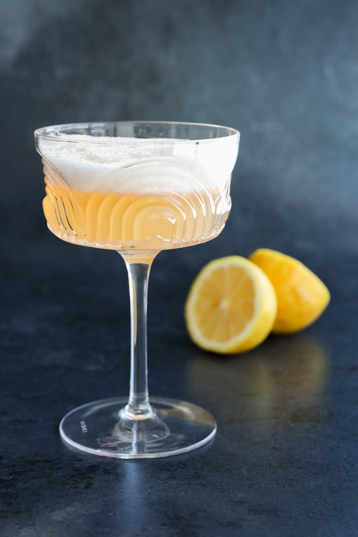 gin sour in coupe glass on black with lemon halves