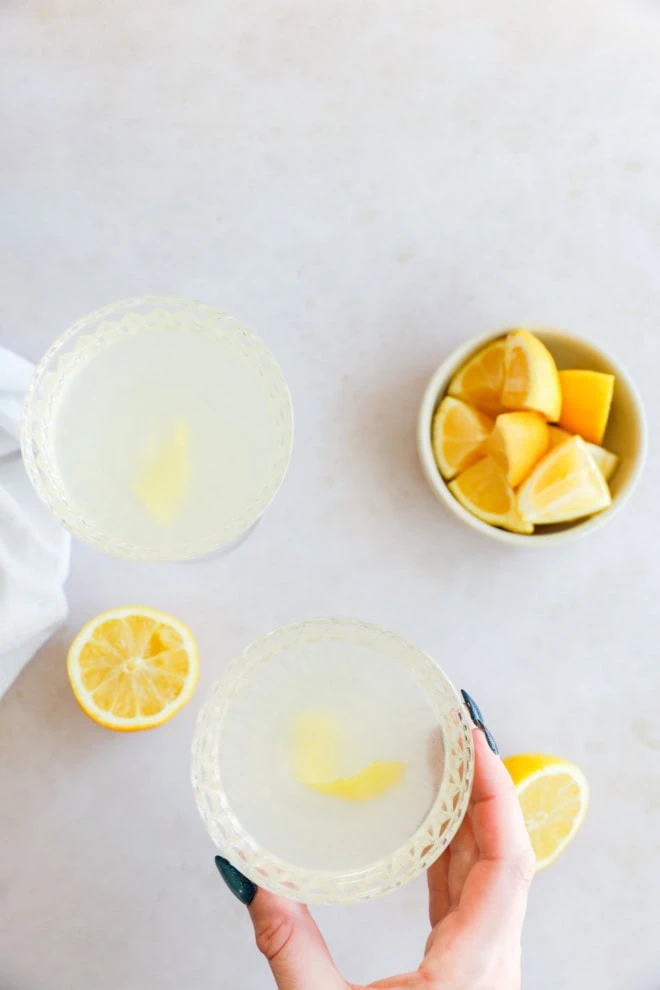 hand holding coupe glass with bees knees cocktail garnished with a lemon twist