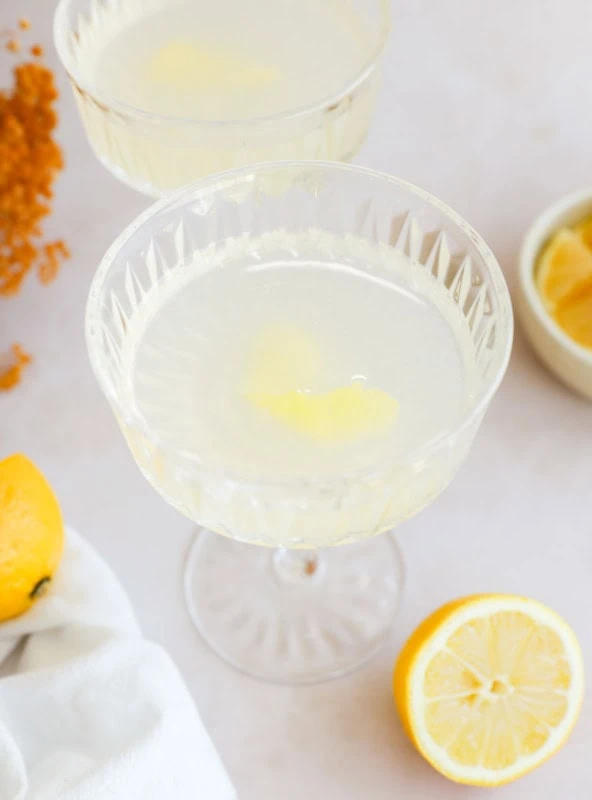 pretty bright lemon cocktail in couple glasses with lemon, white linen, and lemon wedges in a bowl