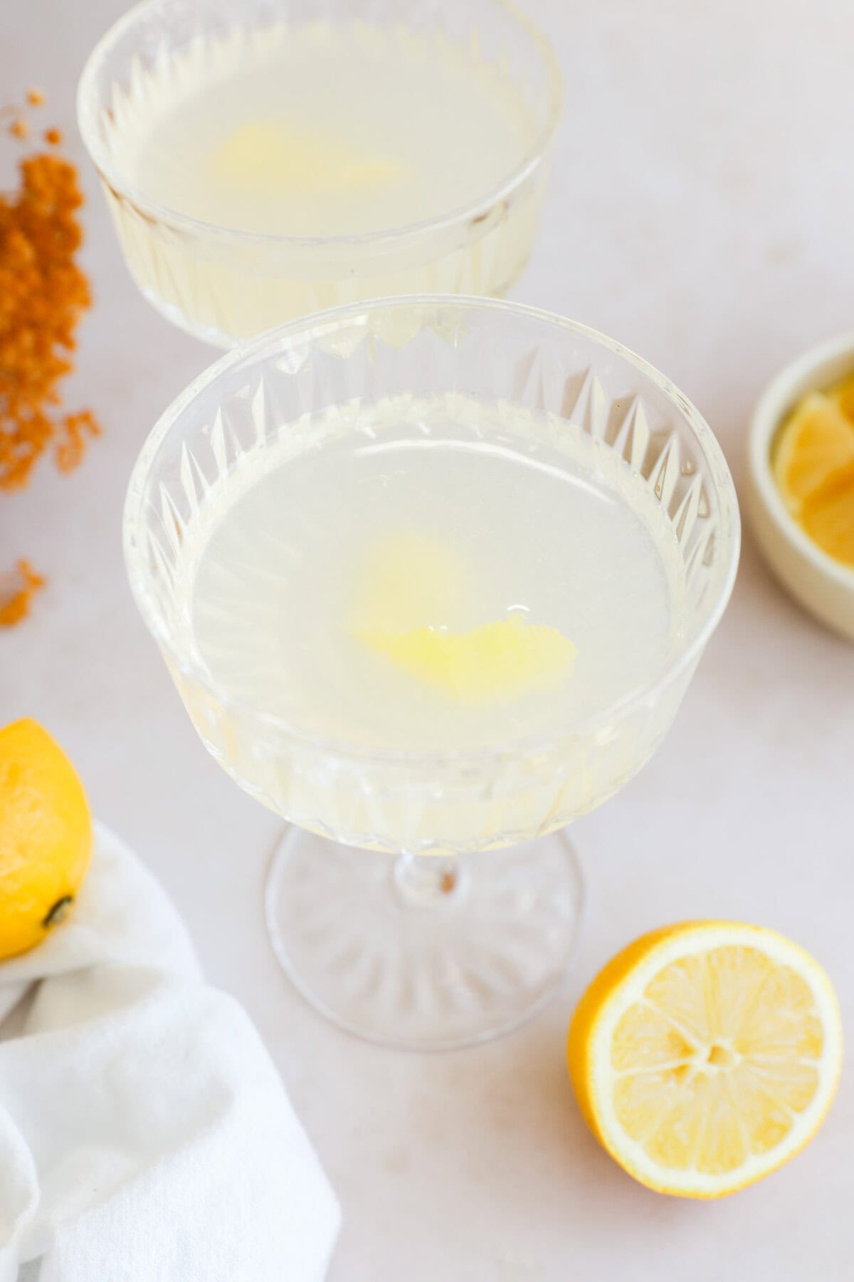 pretty bright lemon cocktail in couple glasses with lemon, white linen, and lemon wedges in a bowl