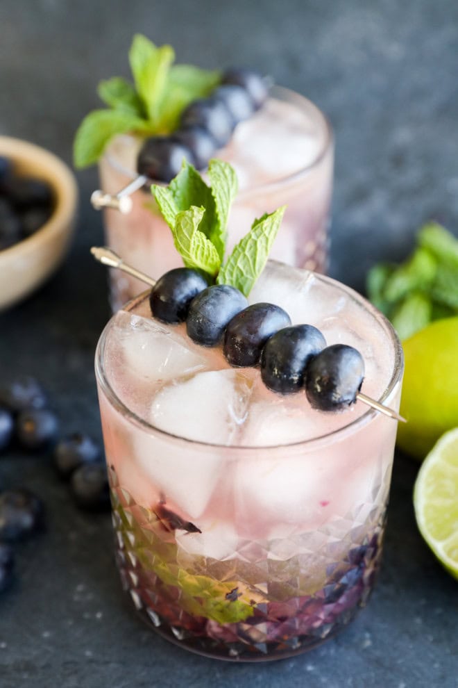 A cocktail glass with blueberry mojito garnished with fresh blueberries and mint leaves