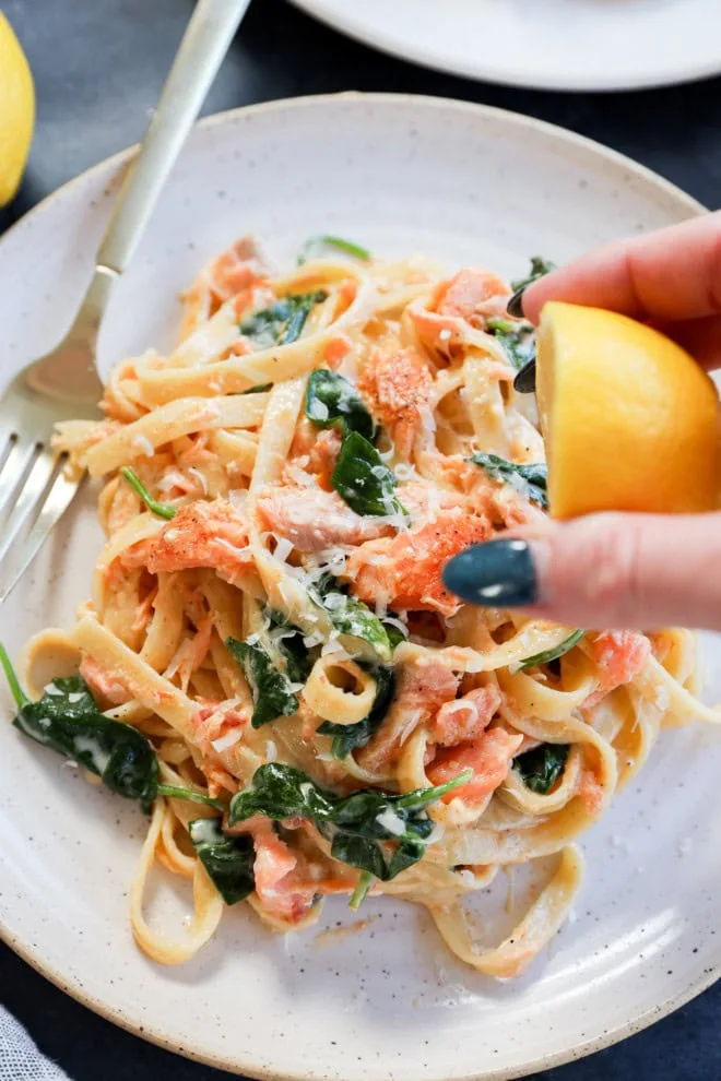 hand squeezing lemon over a plate of creamy fettuccine with seafood and spinach