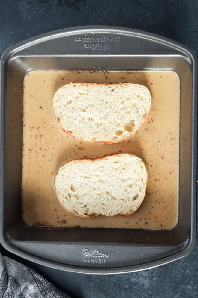 bread slices in custard mix in a shallow baking dish