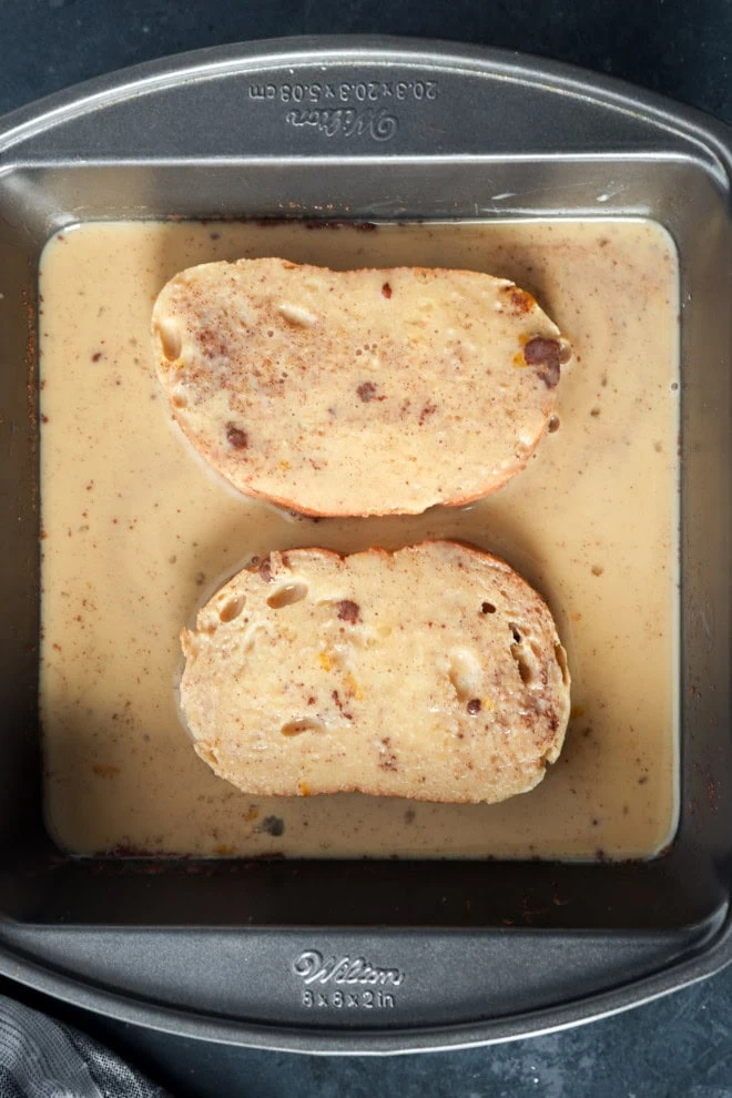 bread slices soaking in egg custard mixture in baking dish