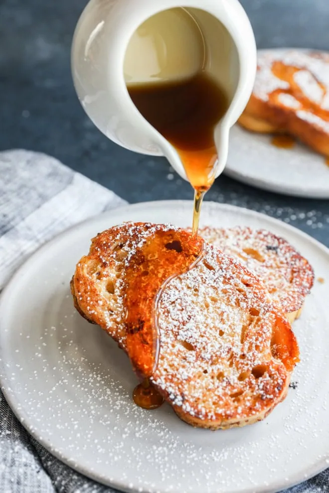 drizzling syrup over slices of sourdough french toast on a plate