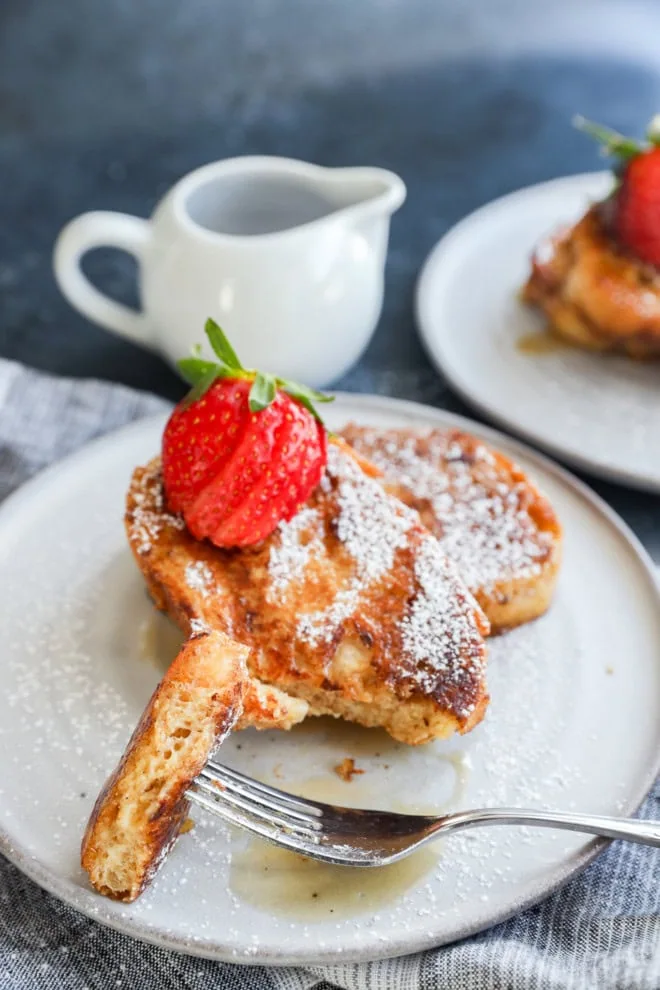 fork taking a bite out of french toast on a plate